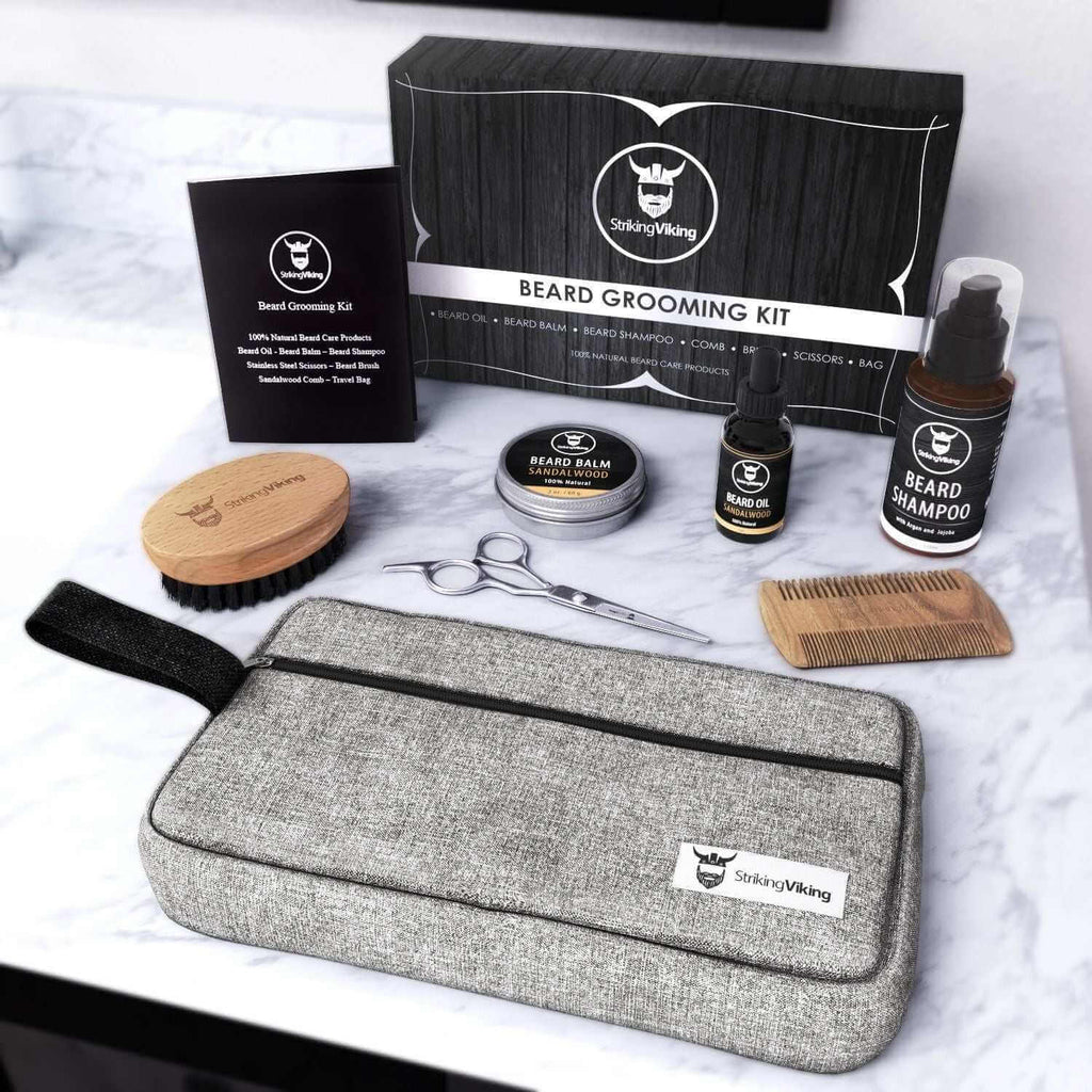 Beard grooming kit for men with shampoo, balm, oil, scissors, brush, comb, toiletry bag, and gift box displayed on a counter.